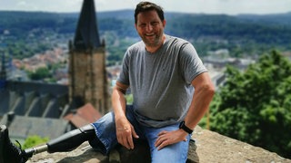 Fritz sitzt auf einer Mauer. Sein rechtes Bein ist amputiert. Er trägt eine Beinprothese. 