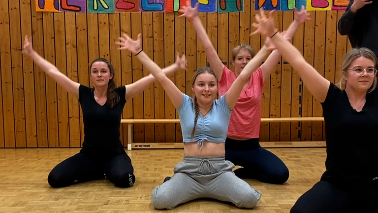 Vier junge Frauen sitzen und strecken die Arme nach oben.