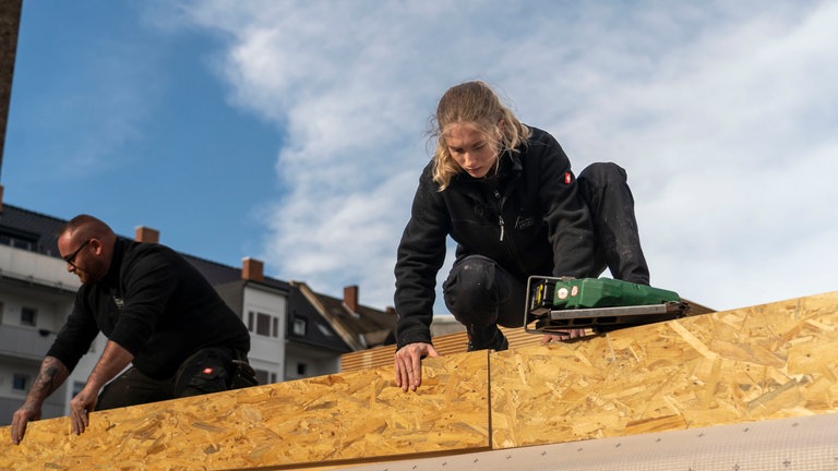 Eine junge Frau hält ein Holzbrett fest und schaut es konzentriert an.