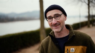 Mittelalter Mann mit Brille lächelt. Er trägt eine dunkle Mütze und ein grünes Fleece.