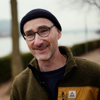 Mittelalter Mann mit Brille lächelt. Er trägt eine dunkle Mütze und ein grünes Fleece.