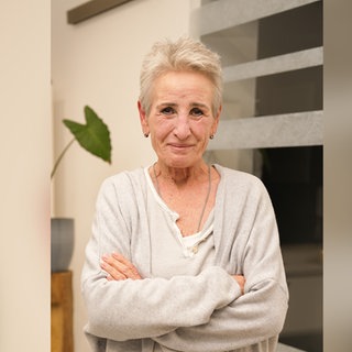 Ältere Dame mit blonden Haaren lächelt leicht in die Kamera.