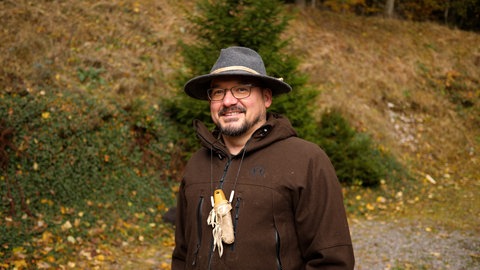 Der Survival Profi Ralf lächelt in die Kamera. Er steht mitten im Wald, sein Revier. 