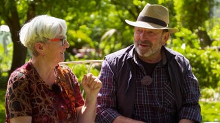 Ein alter Mann und eine alte Frau sitzen auf einer Bank im Garten und unterhalten sich