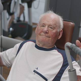 Werner geht mit 97 Jahren zweimal die Woche ins Fitnessstudio. Er trainiert an einem Sportgerät und schaut dabei in die Kamera.