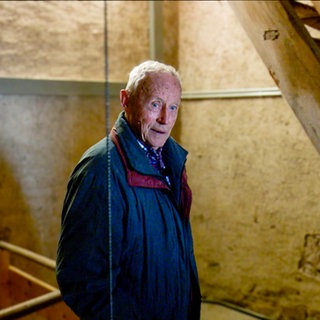 Fritz ist gerade am Treppensteigen im Kirchturm von Görwihl. Man sieht ihn vor einer Treppe und eine Schnur an dem ein Gewicht der Kirchturmuhr hängt.