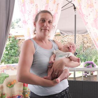 Deborah ist eine Frau Anfang 40, die müde, aber lächelnd in die Kamera schaut. Sie hält ein winziges Baby im Arm.