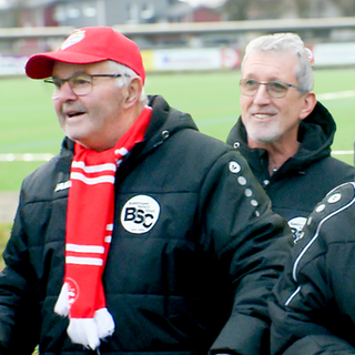 Drei Männer im Rentenalter, die sich im Fußballverein ehrenamtlich engagieren,  stehen am Spielfeldrand und tragen Fan-Artikel des SC Bahlingen.