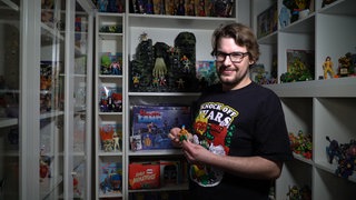 Junger Mann hält eine Actionfigur in der Hand