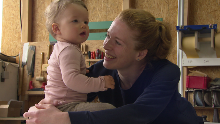 Schreinermeisterin Maxime mit ihrer kleinen Tocher in ihrer Werkstatt