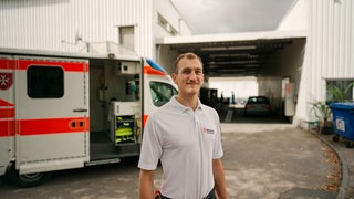 Junger Mann in Sanitäterkleidung vor Krankenwagen