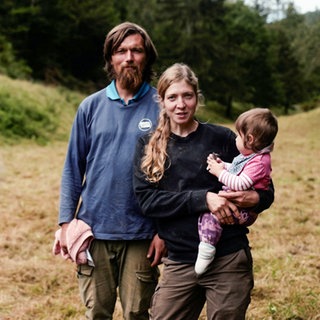 Die Landwirte Leon und Mareike stehen gemeinsam mit ihrer Tochter Sophia, die Mareike im Arm hält, auf einem Feld. Alle drei blicken in die Kamera.