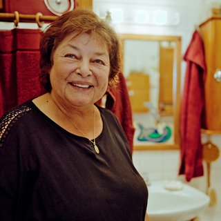 Eine Frau steht in ihrem Badezimmer und lächelt in die Kamera.