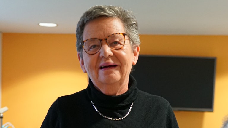 Frau lächelt in die Kamera und hält einen Flyer des Vereins „Hallo-Nachbar“ in der Hand.