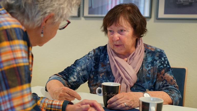Zwei Frauen unterhalten sich an gedecktem Kaffeetisch. 