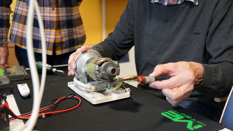 Klaus Thomas repariert ein altes Gerät und tauscht sich dazu mit einer Frau aus. 