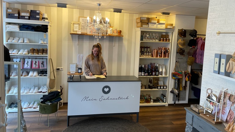 Blonde Frau hinter Theke in einem Laden, schreibt in ein Buch.