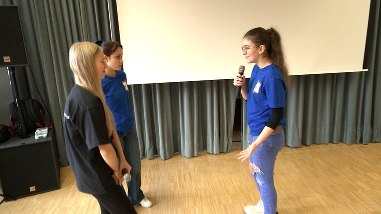 Drei Jugendlichen stehen mit Mikrofon in einem Raum und simulieren eine Szene