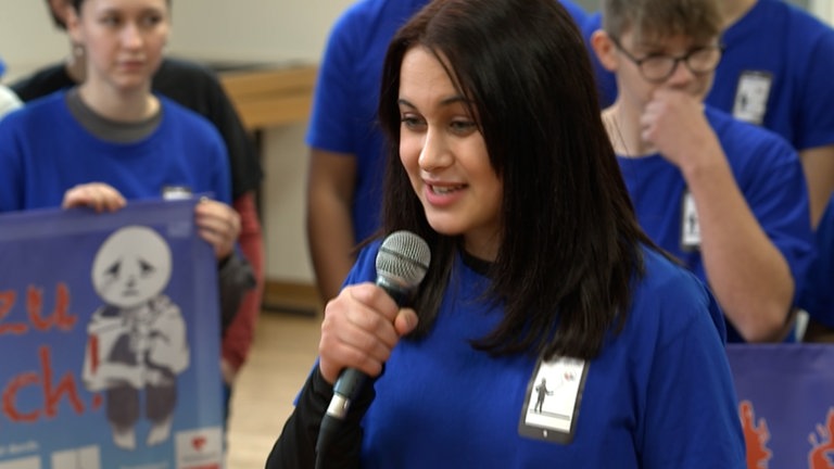 Junge Frau mit schwarten mittellangen Haaren hält ein Mikrofon in der Hand