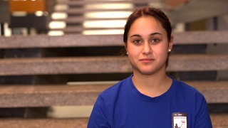 Junge Frau mit schwarzen mittellangen Haaren schaut ernst in die Kamera