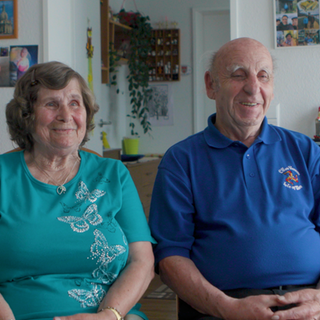 Älteres Ehepaar sitzt nebeneinander und lächelt