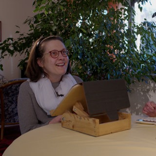 Zwei Frauen sitzen an einem Tisch. Eine trägt eine Brille.