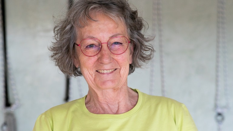 Frau mit Brille und grauen kurzen Haaren lächelt in die Kamera.