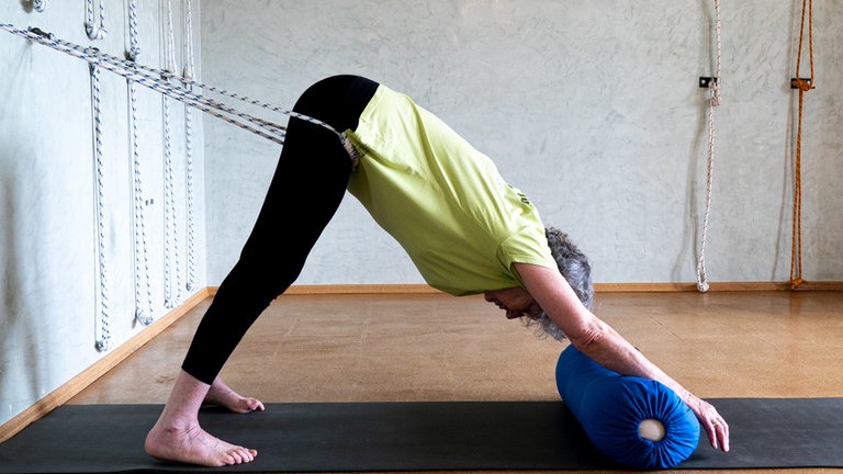 Frau im herabschauenden Hund mit Gurten auf einer Yogamatte mit blauem Sitzsack. 