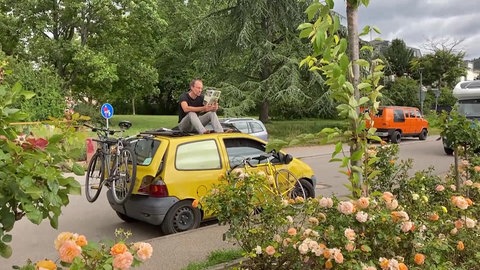 Mann sitzt auf altem Twingo Renault. Es ist sein Tiny-Camper