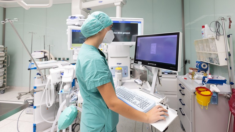 Junge Frau steht im OP und arbeitet an einem Computer.