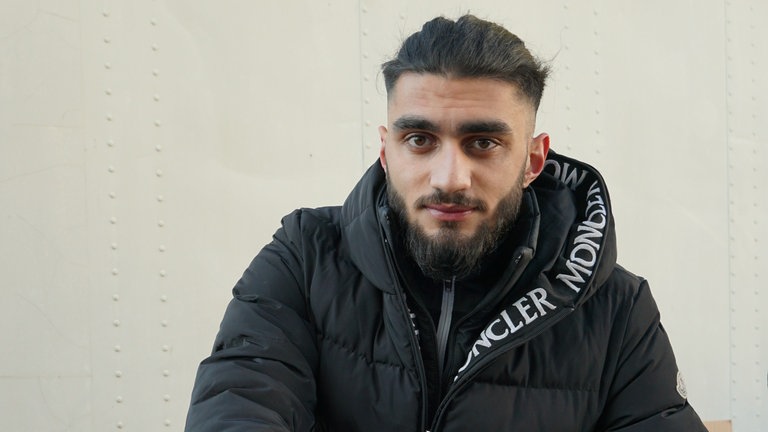 Junger Mann mit schwarzer Jacke, der eine Winterjacke in einen Karton packt. 