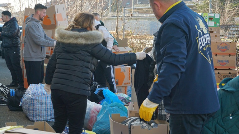 Etliche Menschen, die zwischen großen Umzugkartons stehen.