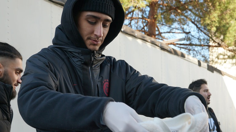 Junger Mann mit Mütze sortiert Kinderkleidung in Kartons.