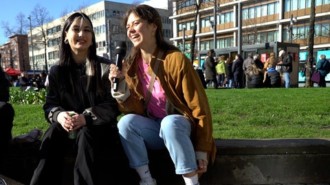 Reporterin sitzt mit junger Frau am Straßenrand
