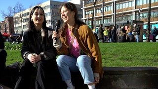 Reporterin sitzt mit junger Frau am Straßenrand