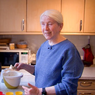 Die 64-jährige Hobby-Köchin Maria steht in ihrer Küche und backt winterliche Apfelmuffins in ihrem Airfryer.