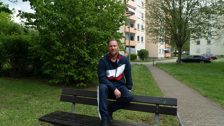 jonny sitzt in Jogginghose auf einer Bank 