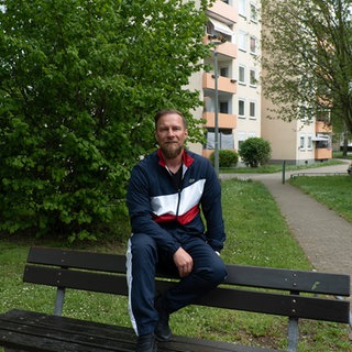 jonny sitzt in Jogginghose auf einer Bank 