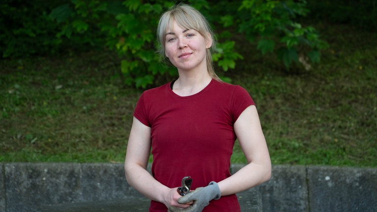 Junge blonde Frau mit rotem T-Shirt, Arbeitshandschuh und Gartenschere.