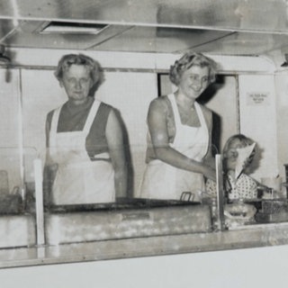 Auf einem alten Schwarz-Weiß-Foto stehen zwei Frauen hinter der Theke eines Imbisswagens. Der Imbiss in St. Goar ist seit fast 60 Jahren Kult.