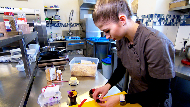Junge Frau dekoriert kleine Törtchen mit essbaren Blumen.