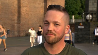 Ein junger Mann mit dunkelblonden Haaren schaut in die Kamera.