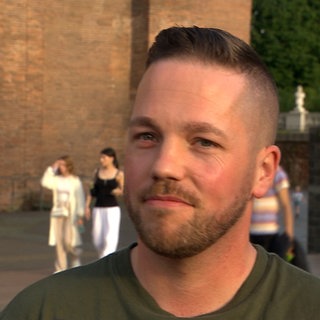 Ein junger Mann mit dunkelblonden Haaren schaut in die Kamera.