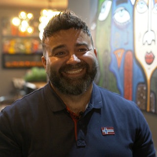 Mann mit schwarzen Haaren und Bart lächelt in Kamera.