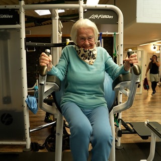 Frau sitzt auf Fitnessgerät und trainiert Arme