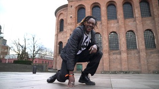 Mann kniet vor Kirche und lacht in die Kamera