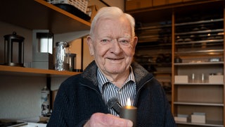 Älterer Herr hält eine kleine Kerze in der Hand und lächelt in die Kamera