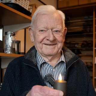 Älterer Herr hält eine kleine Kerze in der Hand und lächelt in die Kamera