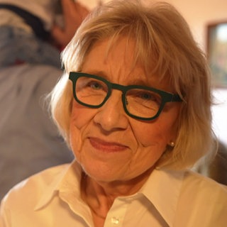 Ältere Dame mit blonden Haaren und Brille lächelt in die Kamera.