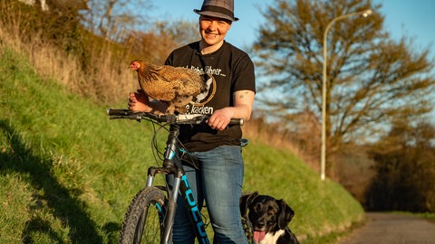 Junge Frau mit Huhn, das auf dem Fahrradlenker sitzt, und einem Hund.